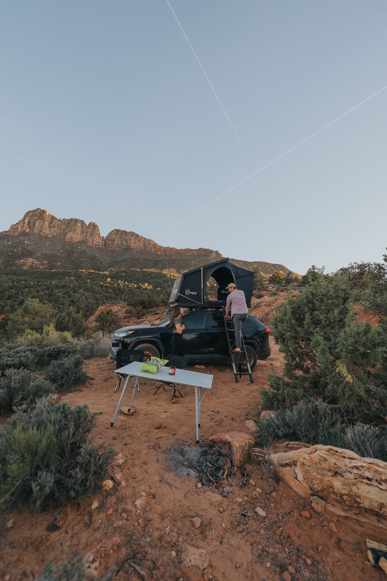 Camp set up beside an Intrepid Geo 2.0 on a black SUV, ladder down at dusk