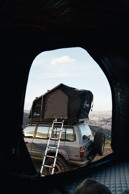 Looking out of a tent at the Intrepid Geo 2.5 on a Land Cruiser with the ladder down