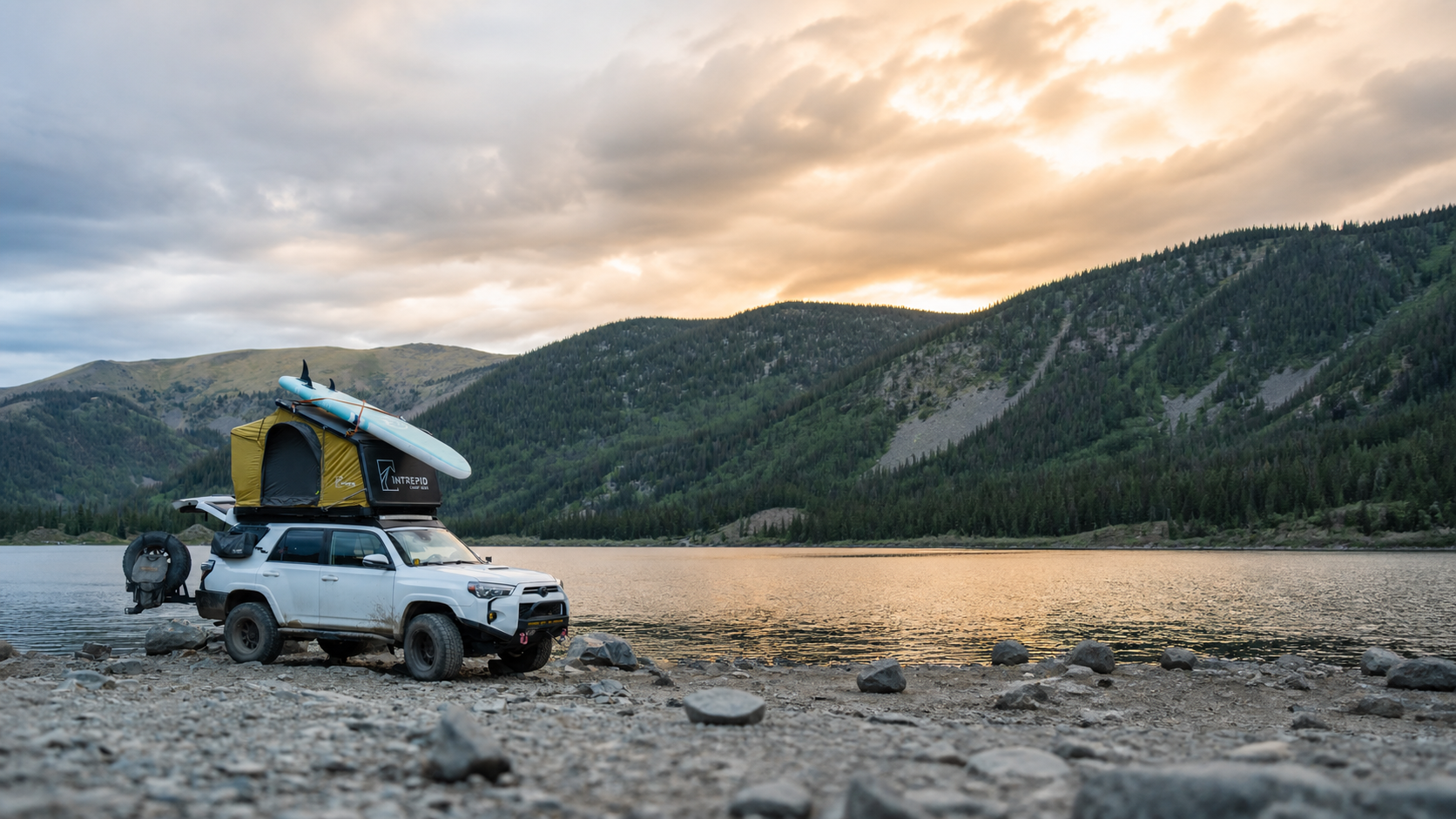 Four-wheel-drive vehicle with a rooftop tent beside an alpine lake